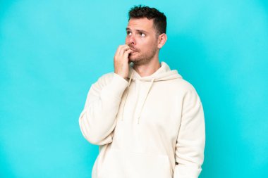 Mavi arka planda izole edilmiş beyaz, yakışıklı genç bir adam biraz gergin.