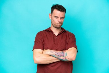 Mutsuz bir ifadeyle mavi arka planda izole edilmiş beyaz, yakışıklı genç bir adam.