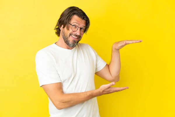 黄色の背景に隔離されたシニアオランダ人男保持コピースペースに挿入する広告 — ストック写真