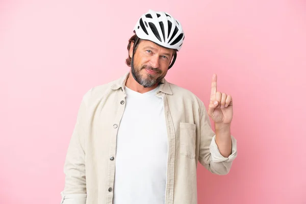 Senior dutch man with bike helmet isolated on pink background showing and lifting a finger in sign of the best
