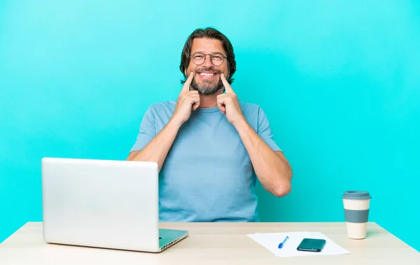 Старший Обов Язковий Чоловік Столом Ноутбуком Ізольований Синьому Фоні Посміхаючись — стокове фото