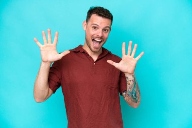 Mavi arka planda izole edilmiş beyaz tenli yakışıklı adam parmaklarıyla 10 'a kadar sayıyor.