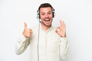 Tele pazarlamacı beyaz arka planda izole edilmiş bir kulaklıkla çalışan beyaz bir adam Tamam işareti ve baş parmak işareti