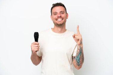 Beyaz arka planda izole edilmiş bir mikrofonu kaldıran beyaz tenli genç şarkıcı en iyinin işareti olarak parmağını kaldırıyor.