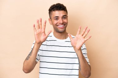 Bej arka planda izole edilmiş genç Brezilyalı adam parmaklarıyla ona kadar sayıyor.