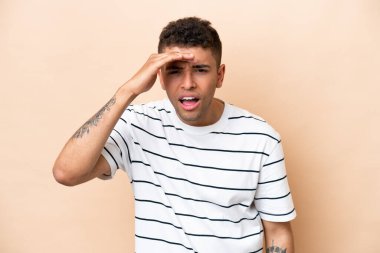 Genç Brezilyalı bir adam bej arka planda izole edilmiş. Bir şeye bakmak için çok uzaklara bakıyor.