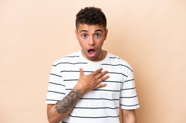 Young Brazilian man isolated on beige background surprised and shocked while looking right