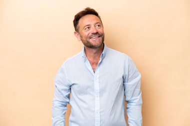 Beyaz tenli orta yaşlı bir adam bej arka planda izole edilmiş bir şekilde yukarı bakarken bir fikir düşünüyor.