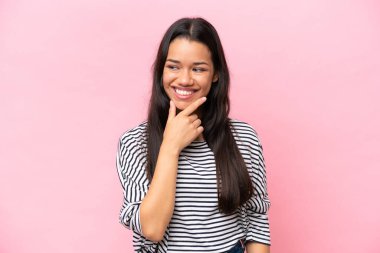 Pembe arka planda soyutlanmış genç Kolombiyalı bir kadın, yana bakıyor ve gülümsüyor.