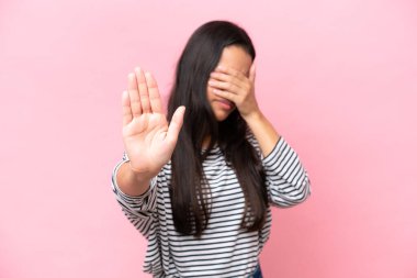 Pembe arka planda izole edilmiş genç Kolombiyalı kadın jesti durdurup yüzünü kapatıyor.