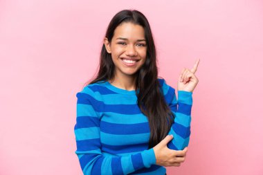 Pembe arka planda izole edilmiş genç Kolombiyalı kadın mutlu ve dik duruyor.