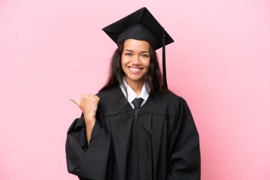 Pembe arka planda tecrit edilmiş genç Kolombiyalı kadın bir ürünü sunmak için kenarı işaret ediyor.