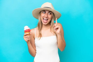 Mavi arka planda izole edilmiş kornet dondurması olan mayo giymiş genç beyaz kadın çözümü fark ederken parmağını kaldırmayı amaçlıyor.