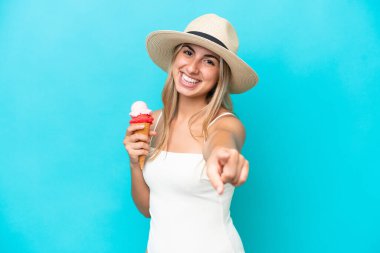 Mavi arka planda izole edilmiş kornet dondurmalı beyaz bir kadın kendine güvenen bir ifadeyle sana işaret ediyor.