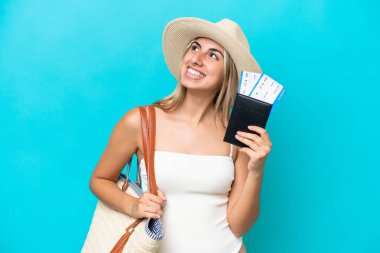 Mayo giymiş, mavi arka planda izole edilmiş pasaportu olan beyaz bir kadın gülümserken yukarı bakıyor.