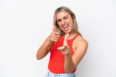 Beyaz arka planda izole edilmiş genç beyaz kadın ön tarafı işaret ediyor ve gülümsüyor.