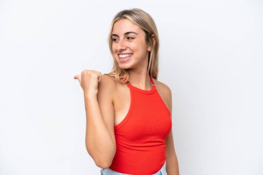 Beyaz arka planda izole edilmiş genç beyaz kadın bir ürünü sunmak için kenarı işaret ediyor.