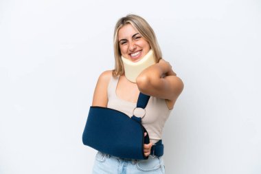 Kırık kollu ve askı takan beyaz arka planda yalnız bir kadın gülüyor.