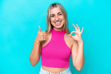 Mavi arka planda izole edilmiş genç beyaz kadın işaret ve baş parmak hareketi gösteriyor.