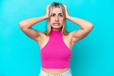 Mavi arka planda izole edilmiş genç beyaz kadın gergin hareketler yapıyor.