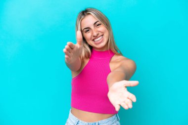 Mavi arka planda izole edilmiş genç beyaz kadın sunar ve davet eder.