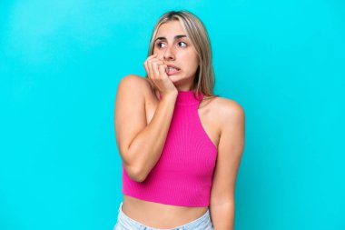 Mavi arka planda izole edilmiş genç beyaz kadın biraz gergin.