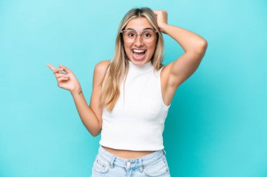 Mavi arka planda izole edilmiş genç beyaz kadın şaşırdı ve işaret etti.