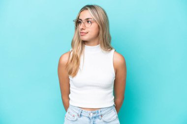 Mavi arka planda izole edilmiş genç beyaz kadın yan tarafa bakıyor.