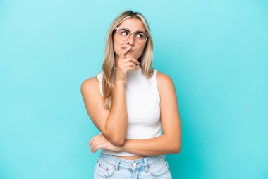 Kafkasyalı genç bir kadın mavi arka planda izole edilmiş. Şüpheleri var ve kafası karışmış bir yüz ifadesi var.