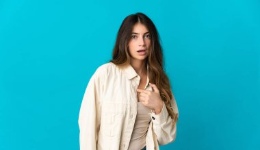 Mavi arka planda izole edilmiş genç beyaz kadın kendini işaret ediyor.