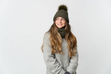 Young caucasian woman with winter hat isolated on white background looking to the side and smiling