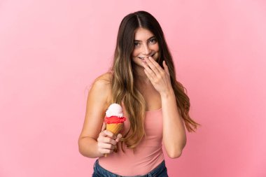Kornet dondurması olan beyaz bir kadın pembe arka planda izole edilmiş mutlu ve gülümseyen elleriyle ağzını kapatıyor.