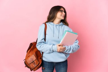 Young student woman isolated on pink background looking to the side and smiling