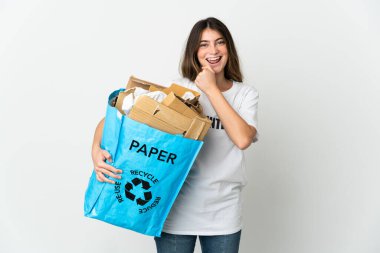 Bir zaferi kutlamak için beyaz arka planda izole edilmiş, kağıt dolu bir geri dönüşüm çantası tutan genç bir kadın.