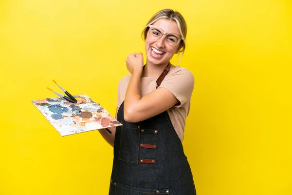 年轻的艺术家卡西亚女人拿着一个黄色背景的调色板庆祝胜利 — 图库照片