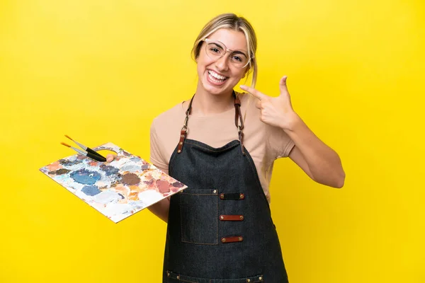 黄色の背景に孤立したパレットを持つ若い芸術家の白人女性は 親指を立てるジェスチャーを与えます — ストック写真