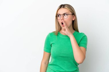 Beyaz arka planda izole edilmiş genç beyaz kadın yan tarafa bakarken sürpriz bir jest yaparak bir şeyler fısıldıyor.