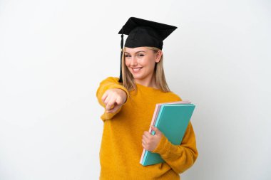 Beyaz arka planda izole edilmiş genç beyaz kadın, mutlu bir ifadeyle ön tarafı işaret ediyor.