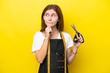 Young seamstress English woman isolated on yellow background having doubts and thinking