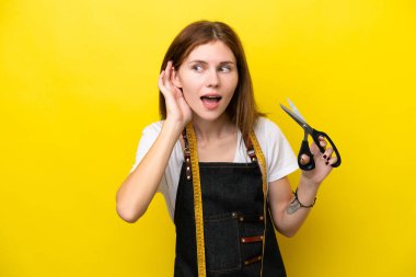 Genç terzi kadın sarı arka planda izole edilmiş bir şekilde elini kulağına koyarak bir şeyler dinliyor.