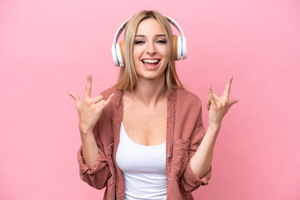 Pretty blonde woman isolated on pink background listening music making rock gesture