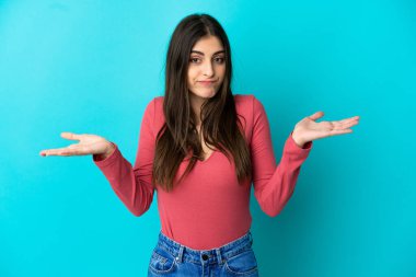 Mavi arka planda izole edilmiş genç beyaz kadın ellerini kaldırırken şüpheleri var.