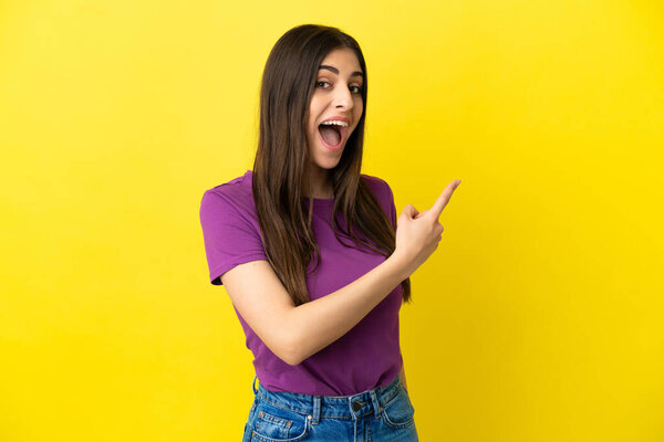 Young caucasian woman isolated on yellow background surprised and pointing side