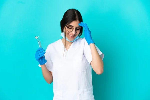 年轻的高加索牙医女人拿着用蓝色背景笑隔离的工具 — 图库照片