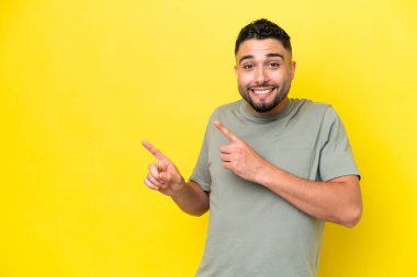 Sarı arka planda izole edilmiş genç ve yakışıklı bir adam korkmuş ve kenarı işaret ediyor.