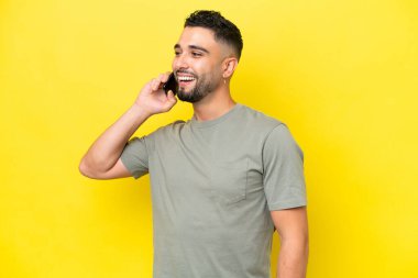 Genç Arap yakışıklı adam sarı arka planda izole edilmiş cep telefonuyla sohbet ediyor.