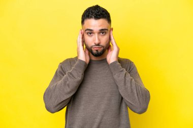 Sarı arka planda izole edilmiş genç Arap yakışıklı adam hayal kırıklığına uğramış ve kulaklarını kapatmış.