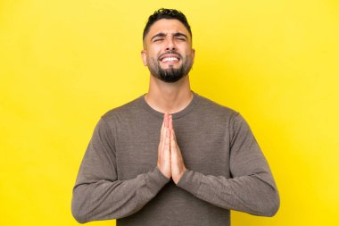 Sarı arka planda izole edilmiş genç Arap yakışıklı adam avuç içlerini bir arada tutuyor. İnsan bir şey ister.