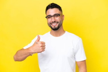 Young Arab handsome man isolated on yellow background With glasses and with thumb up