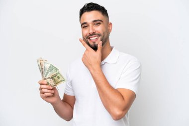 Genç bir Arap, beyaz arka planda izole edilmiş bir sürü para alıyor. Mutlu ve gülümsüyor.